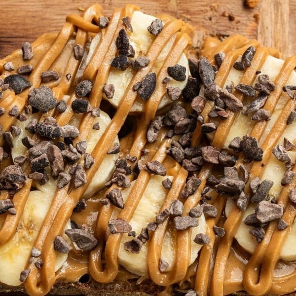 Close-up of banana slices, peanut butter drizzle, and chocolate nibs on toast.