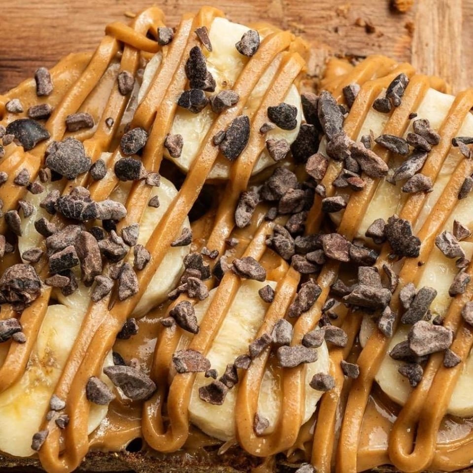 Close-up of banana slices, peanut butter drizzle, and chocolate nibs on toast.
