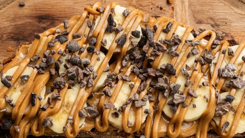Close-up of banana slices, peanut butter drizzle, and chocolate nibs on toast.