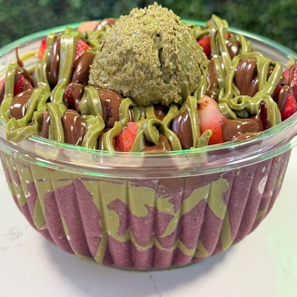 A vibrant acai bowl topped with strawberries, chocolate drizzle, and a scoop of pistachio cream.