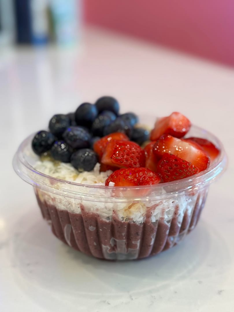 A vibrant acai bowl topped with fresh blueberries, sliced strawberries, and shredded coconut.