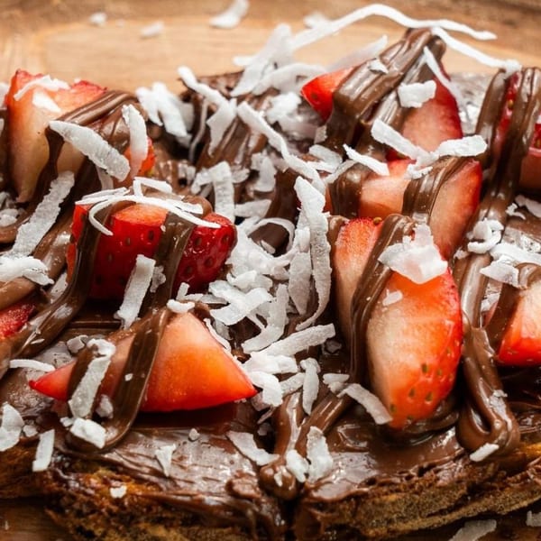 Close-up of chocolate spread on toast, topped with sliced strawberries and shredded coconut.