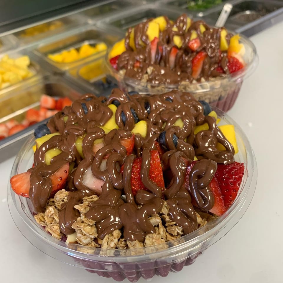Two fruit bowls topped with granola, strawberries, blueberries, mango, and chocolate drizzle.