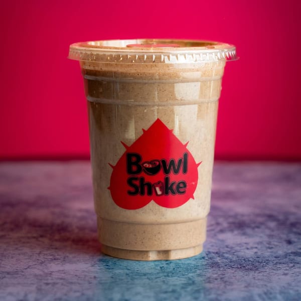 A Bowl Shake branded smoothie in a clear plastic cup against a vibrant red background.