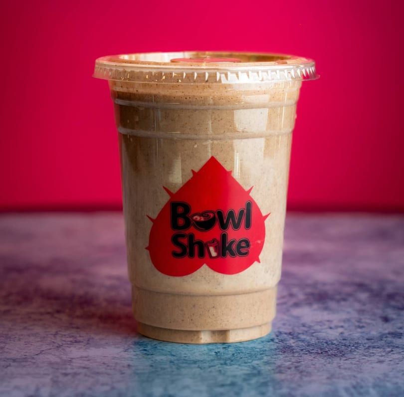A Bowl Shake branded smoothie in a clear plastic cup against a vibrant red background.